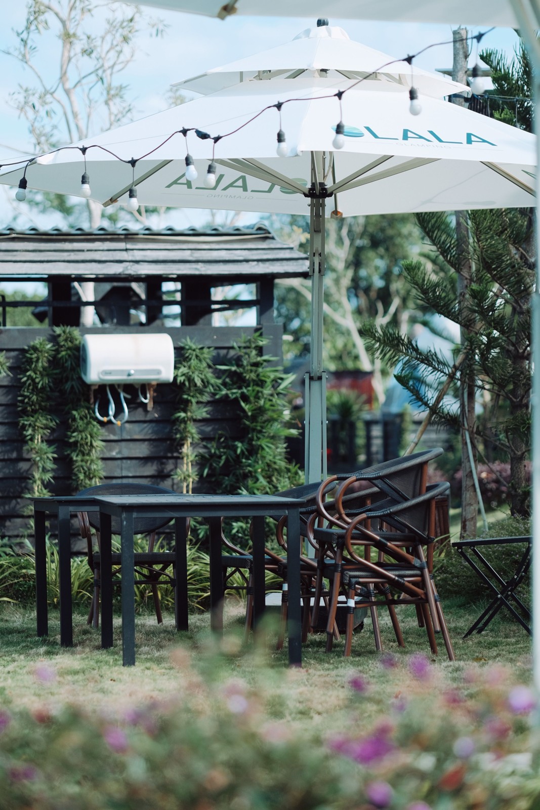 An umbrella stands beside garden seating in a planted patio; it illustrates canopy placement and is not identified as any reviewed product.