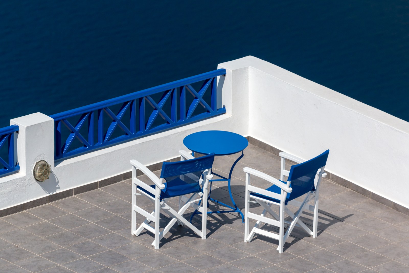 Two chairs and a round table on a sunny terrace in Fira